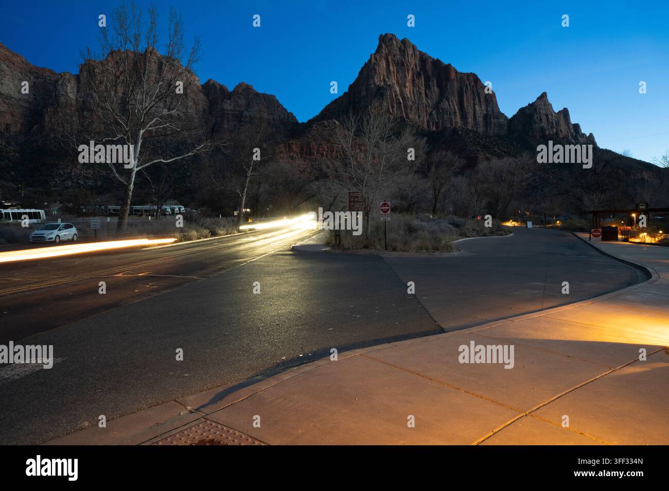 Autos erzeugen Lichtstreifen auf der Zion-Mount Carmel Highway im Zion-Nationalpark in der Dämmerung, eingerahmt vom The Watchman-Gipfel. Stockfoto