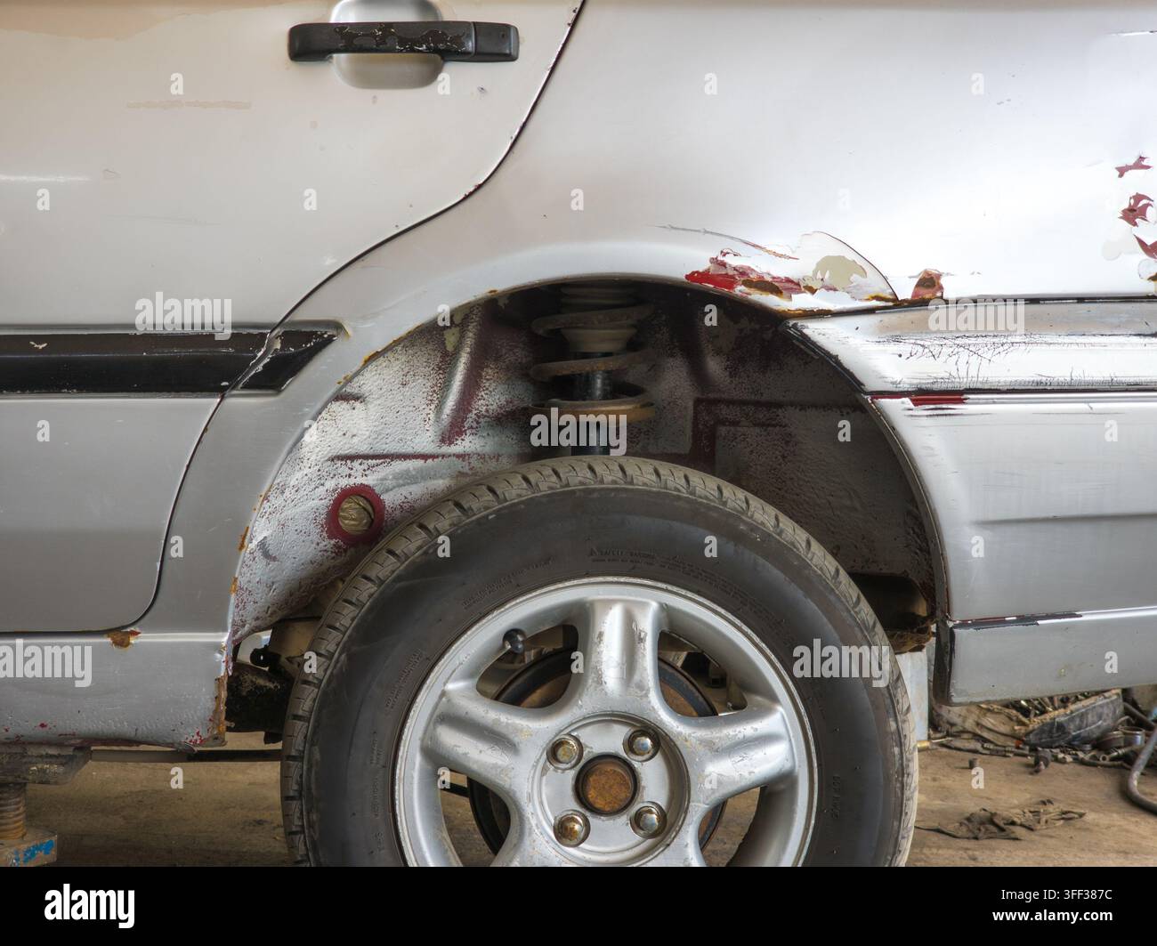Nahaufnahme des hinteren Radkessels und der Tür eines silbernen Autos, die Rost und Lackschäden aufweisen. Die Szene deutet auf Autoreparatur mit sichtbaren Aufhängungskomponenten hin. Stockfoto