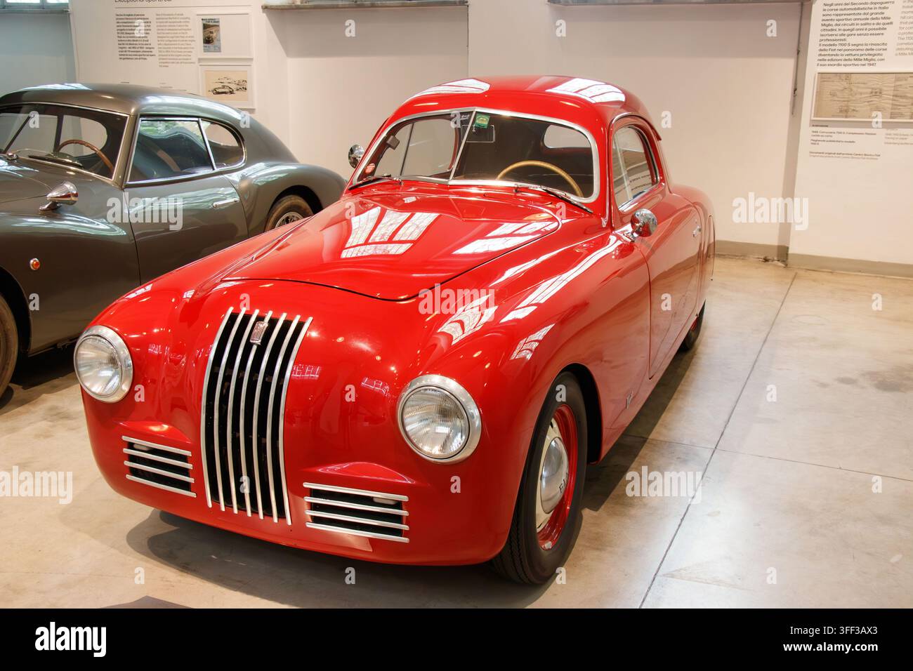 Klassischer roter Fiat 500 Topolino in einer Indoor-Museumsausstellung mit Informationspanelen und benachbarten klassischen Fahrzeugen Stockfoto