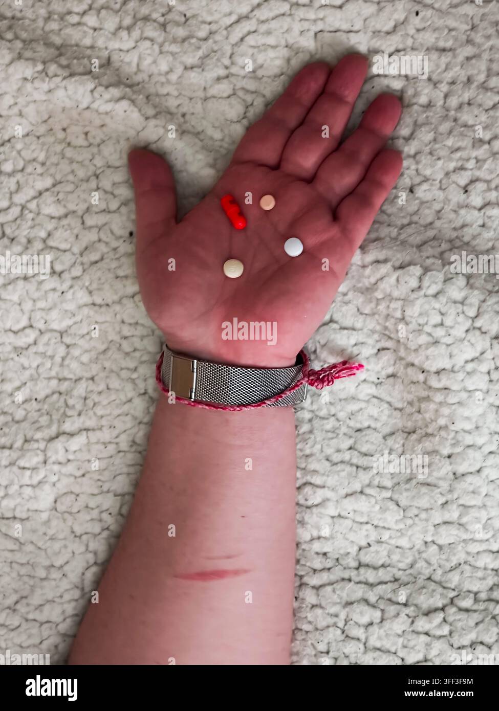 Die Hand hält verschiedene verschreibungspflichtige Medikamente, einschließlich Kapseln und Tabletten, die sichtbare Narben des Selbstschadens am Unterarm zeigen, die geistiges HE darstellen Stockfoto