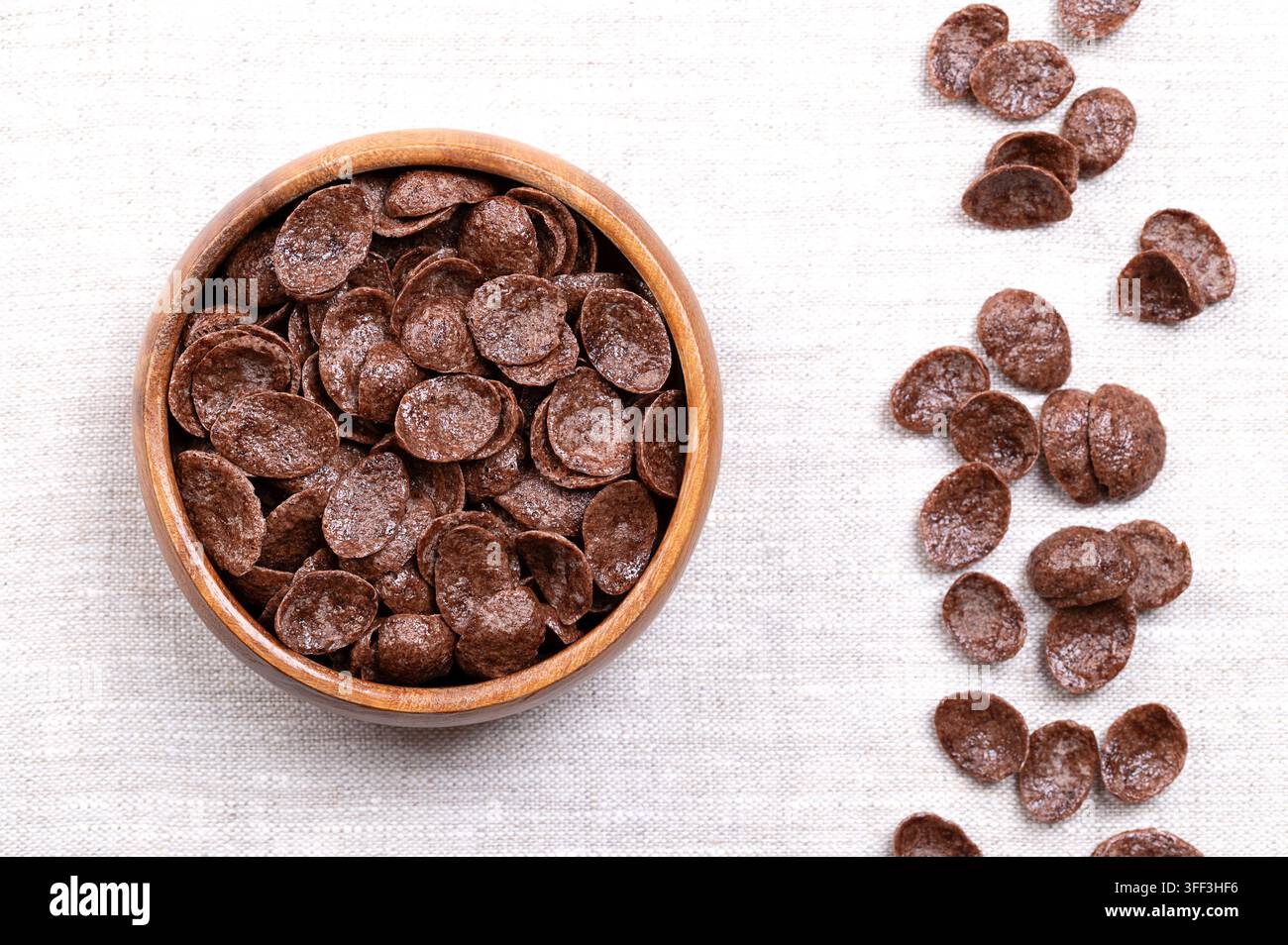 Schokoplätzchen, knuspriges Frühstücksgetreide in einer Holzschüssel auf Leinen. Knuspriges Weizenprodukt aus geröstetem Weizenmehl, Kakaopulver und mit Zucker gesüßt. Stockfoto