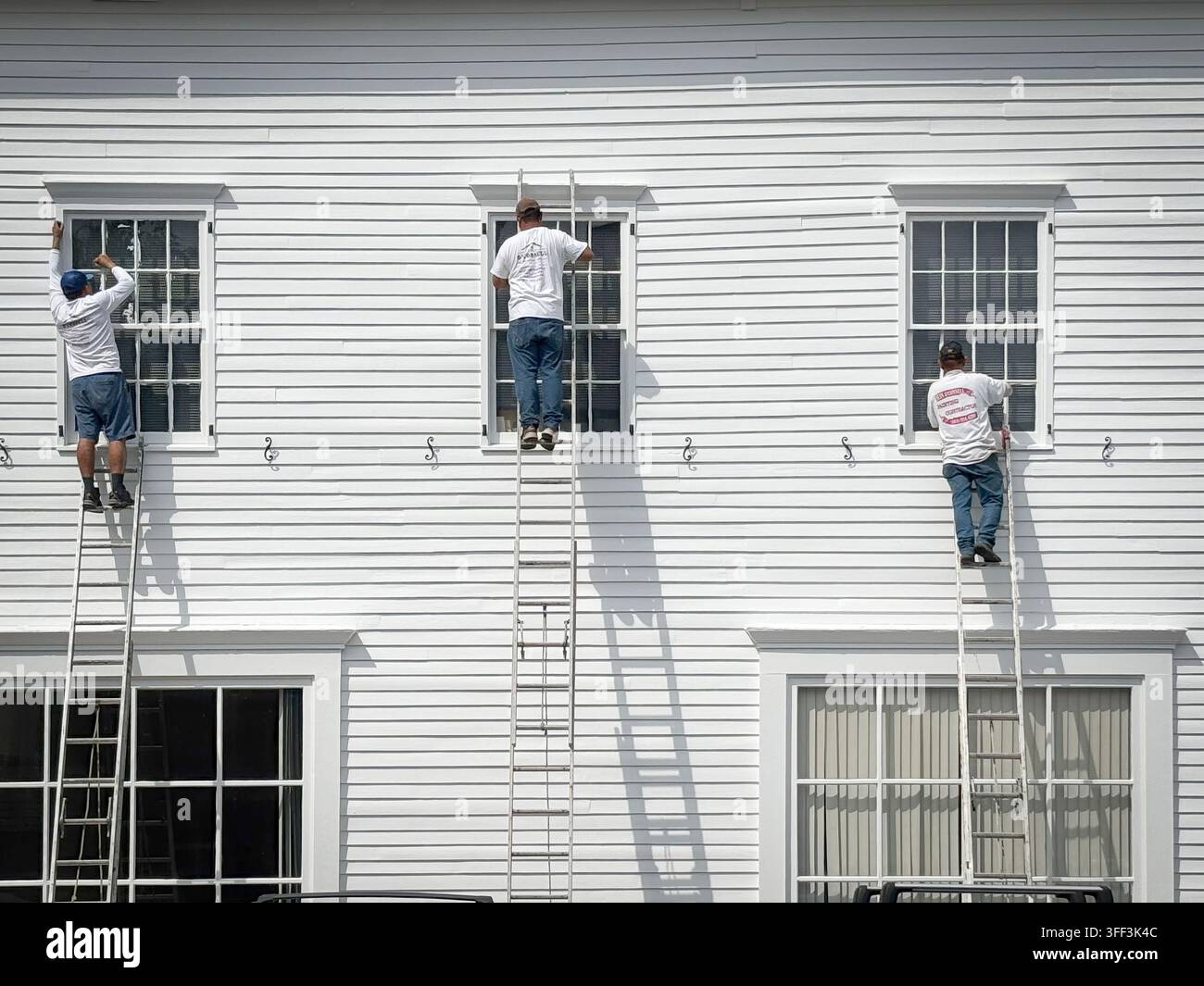 3 Maler malen Fensterrahmen & Schienen, während sie hoch oben auf Leitern stehen. Im Norden des Bundesstaates New York. Stockfoto