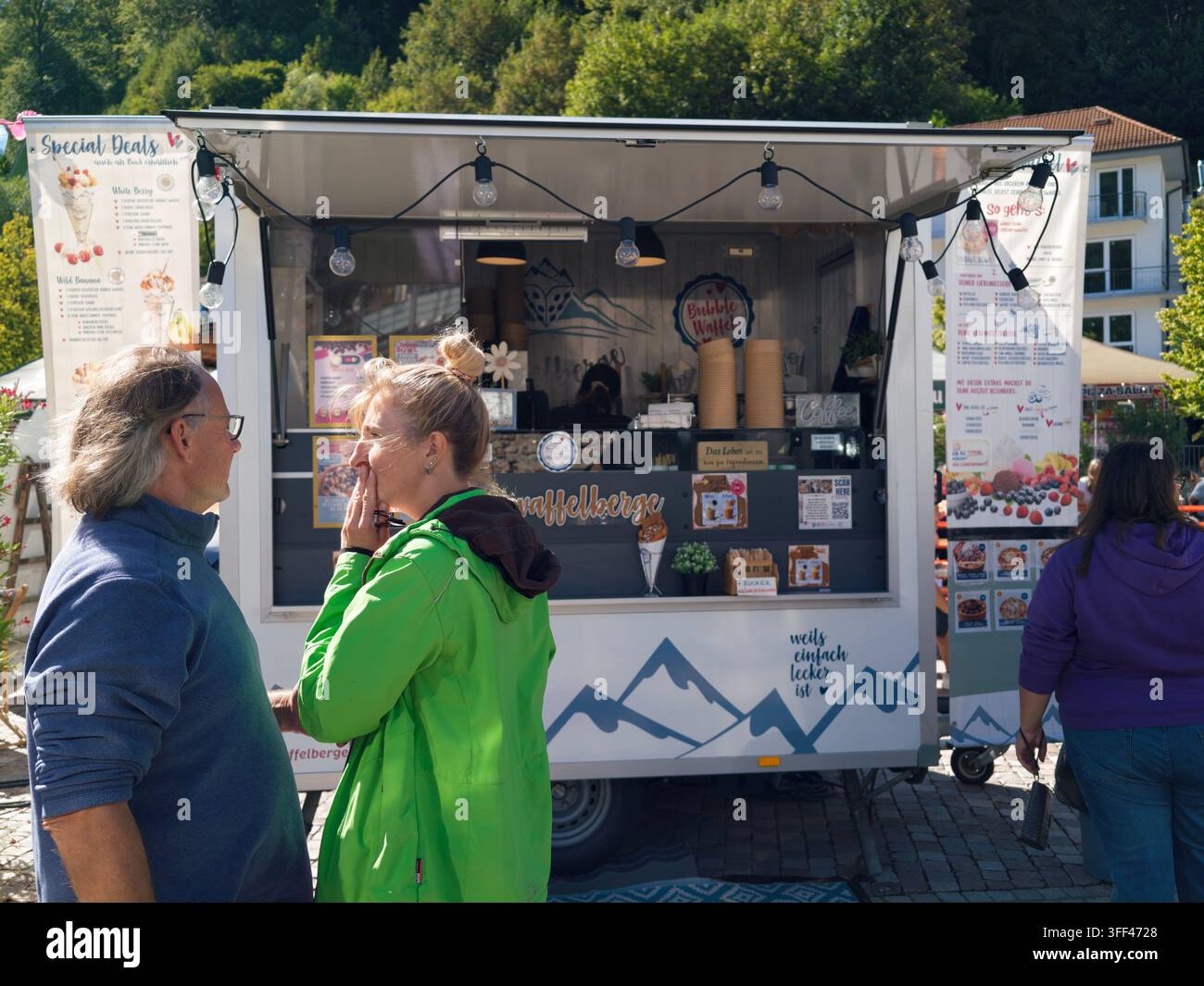 Bad Herrenalb, Deutschland, 5. September 2026: Outdoor-Straßenmarkt an einem sonnigen historischen Platz mit Foodtrucks, schattigen Außentischen, Gästen, Kopfsteinpflaster Stockfoto