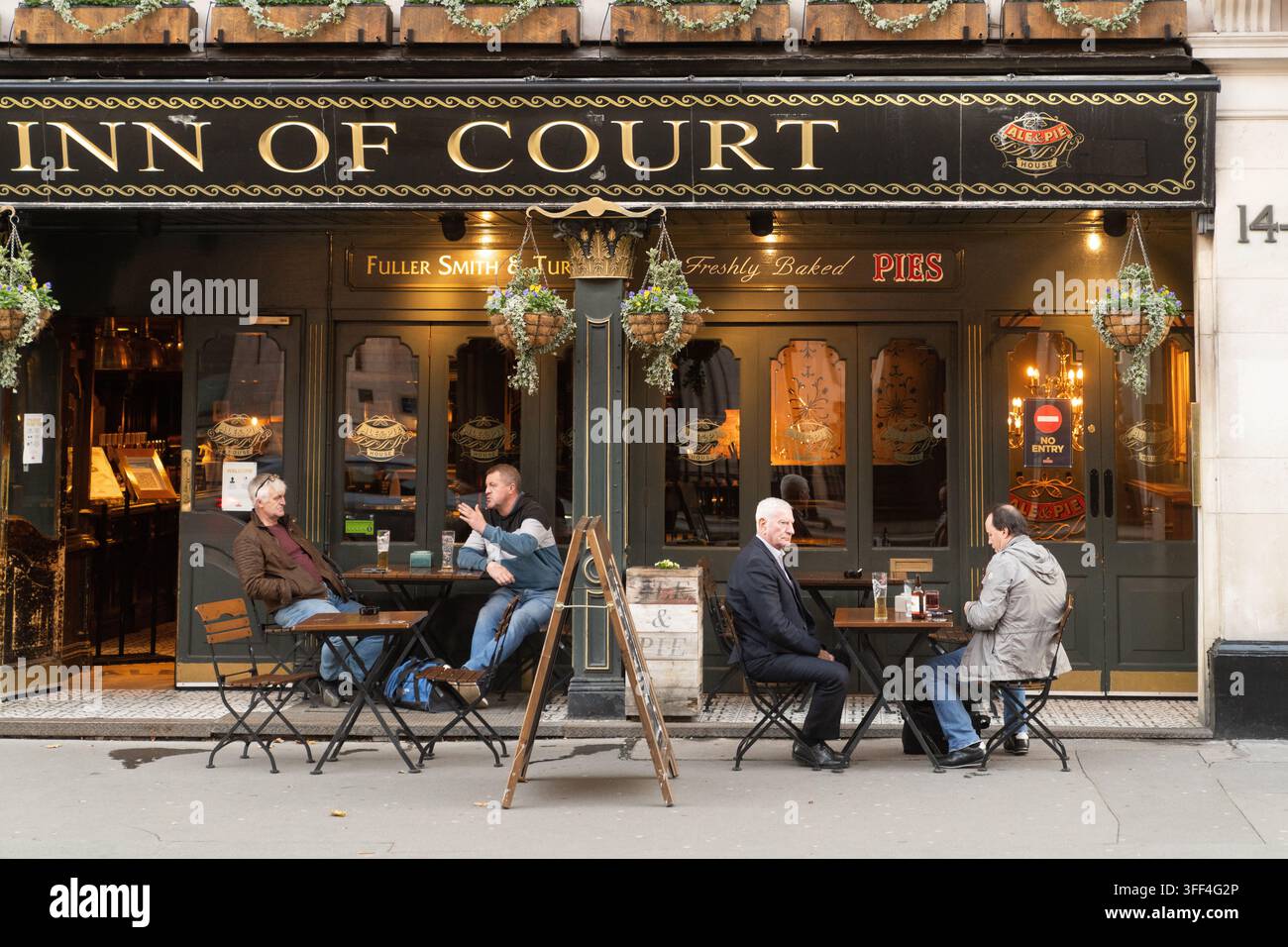 Vier Gäste entspannen sich mit Getränken vor dem Inn of Court Pub in High Holborn, London, und genießen einen geselligen Nachmittag. Stockfoto