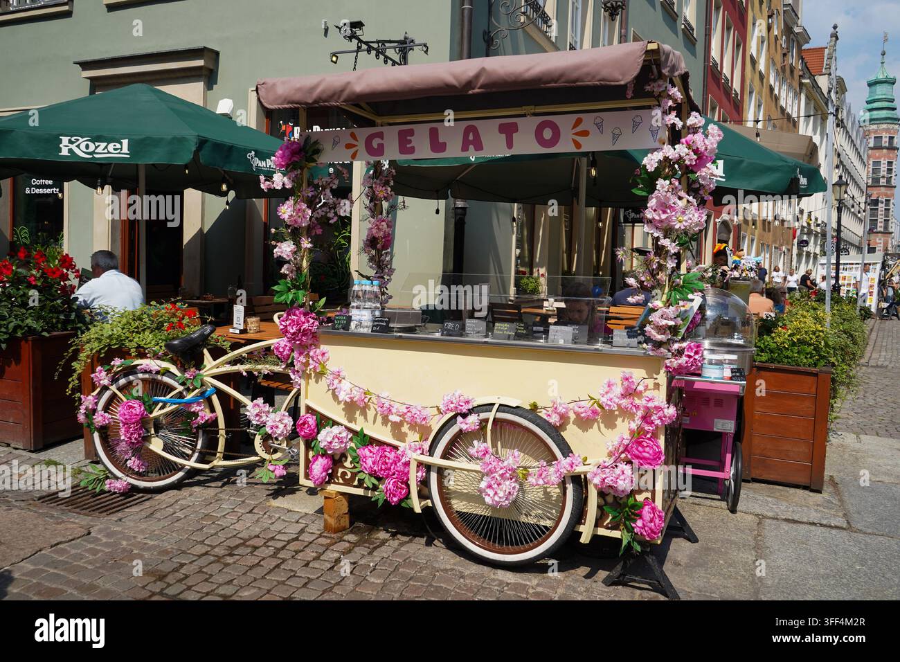 Dekorativer Blumeneiswagen auf Rädern, der auf einer Straße in der Nähe von Außencafés in Danzig, Polen, geparkt ist. Stockfoto