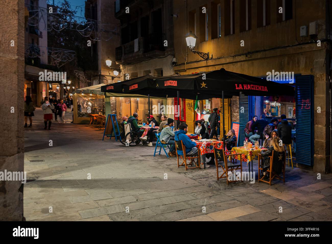Abendliche Straßencafé-Szene in Barcelona mit Gästen und warmen Straßenlaternen Stockfoto