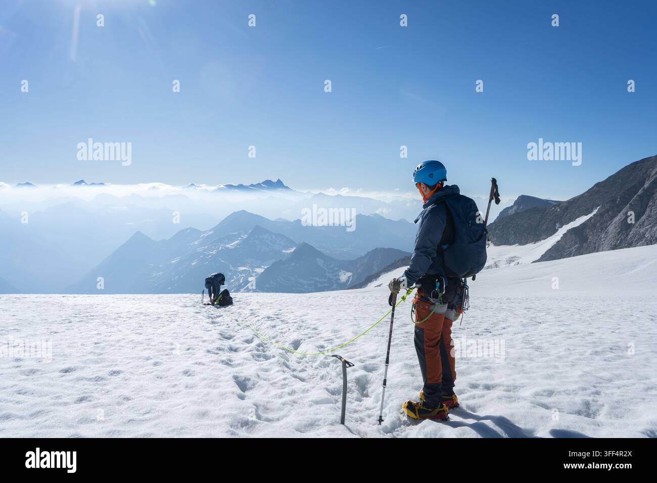 Bergsteiger, der auf einem schneebedeckten Gletscher mit Seil gesichert ist und auf die weite Alpenpanorama blickt, Großvenediger, Österreich Stockfoto