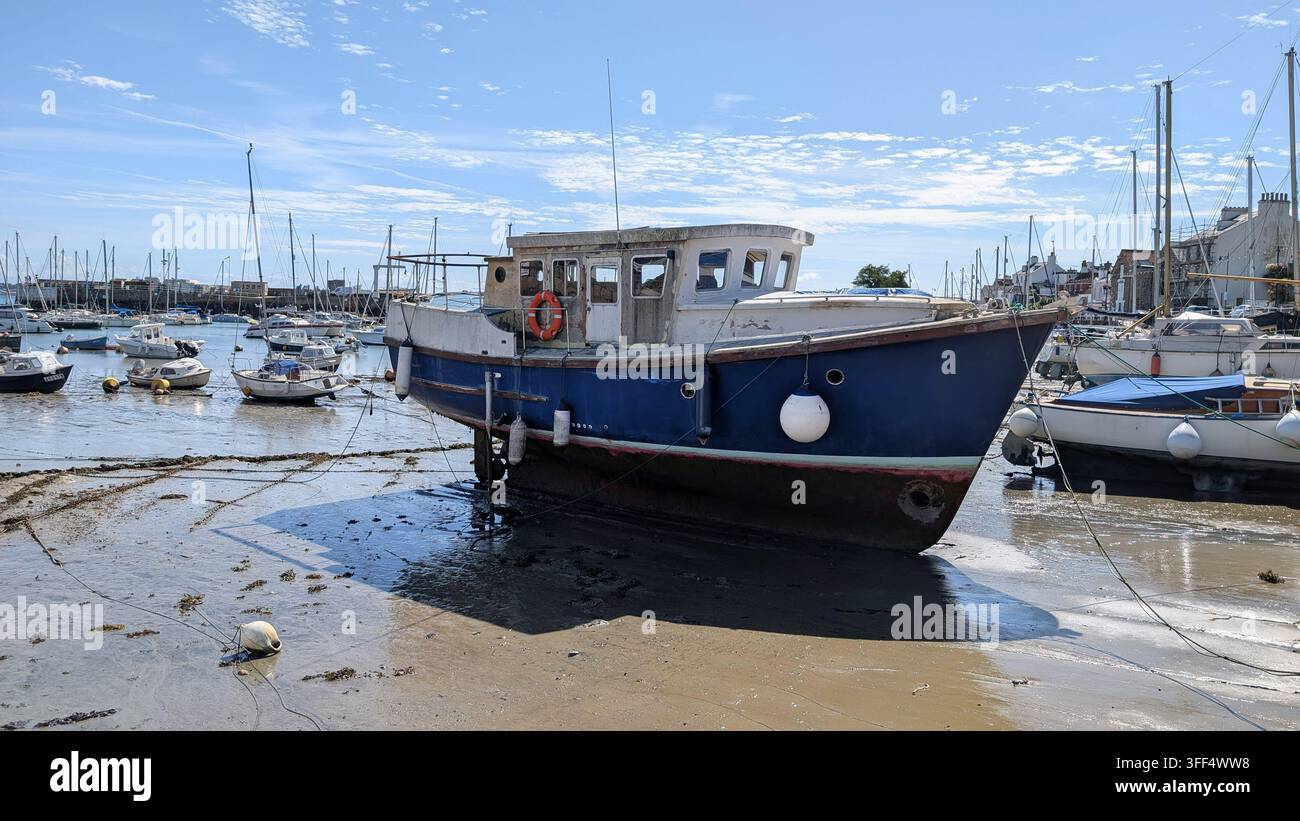 St Aubin, Jersey, Kanalinseln – 31. August 2026: Ein verwittertes Boot ruht auf dem freiliegenden Hafenbett bei Ebbe in St Aubin’s Hafen. Stockfoto