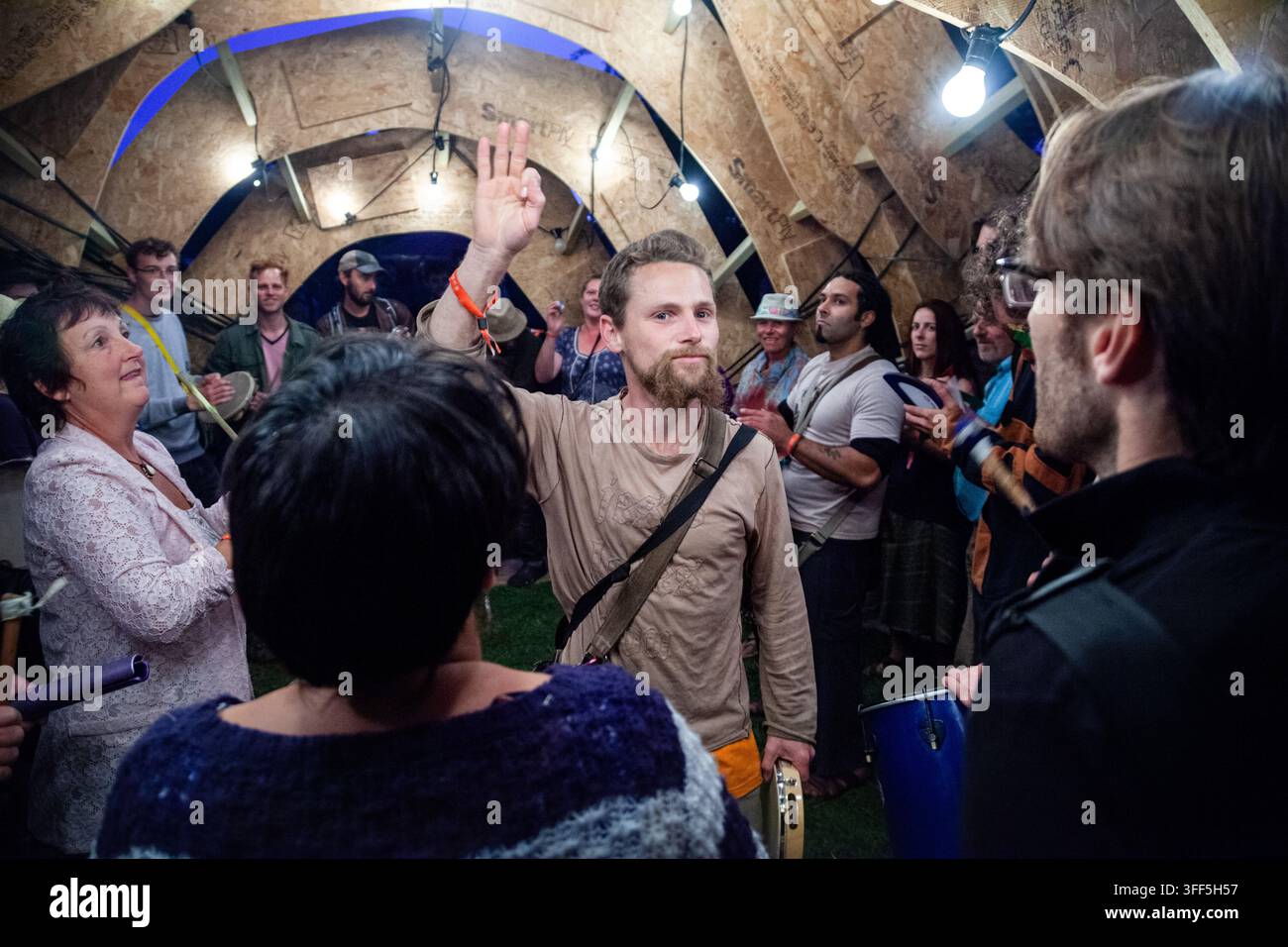 GEMEINSCHAFTSDRUMMSESSION IN EINER SKULPTUR AUF EINEM FESTIVAL, REPORTAGE, GREEN MAN FESTIVAL 2013, BRECON, WALES, UK, 2013: Eine vielfältige Gruppe von lächelnden Menschen verschiedenen Alters steht eng beieinander in einer gebogenen Holzskulptur und spielt energisch Trommeln und schüttelt Schlaginstrumente. Foto: Rob Watkins. INFO: Das Green Man Festival findet jährlich im August in den Brecon Beacons statt. Es feiert alternative Musik, Kunst, Literatur, Wissenschaft und familienfreundliche Kultur in einer wunderschönen Berglandschaft. Das Event 2013 war die 10. Jubiläumsausgabe. Stockfoto