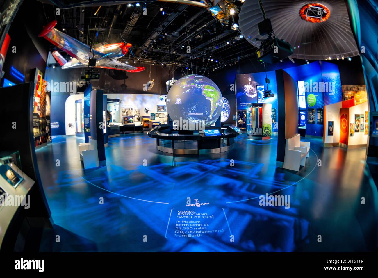 One World Connected Galerie im Luft- und Raumfahrtmuseum | WASHINGTON D.C., Vereinigte Staaten — Ein rotierender Globus verfolgt umlaufende Satelliten in der One World Connected Galerie im National Air and Space Museum, wobei ein rotes Rennflugzeug über ihm schwebt. Die Bodendarstellung markiert die mittlere Erdumlaufbahn des Globalen Positionierungssystems in etwa 12.550 Meilen (20.200 km) über dem Planeten und veranschaulicht, wie Satellitenkonstellationen die moderne Navigation unterstützen. Die Galerie zeigt, wie Luftfahrt- und Raumfahrttechnologie die globale Kommunikation und das Alltagsleben geprägt haben. Stockfoto