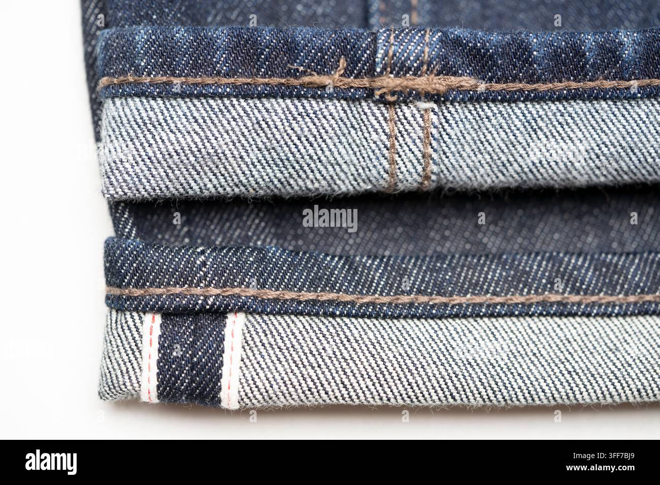 Selvedge-Denimjeans von Uniqlo mit roter Ohrnähte auf weißem gewebtem Selbstrand (unten) reguläre Uniqlo-Denimjeans (oben) Stockfoto