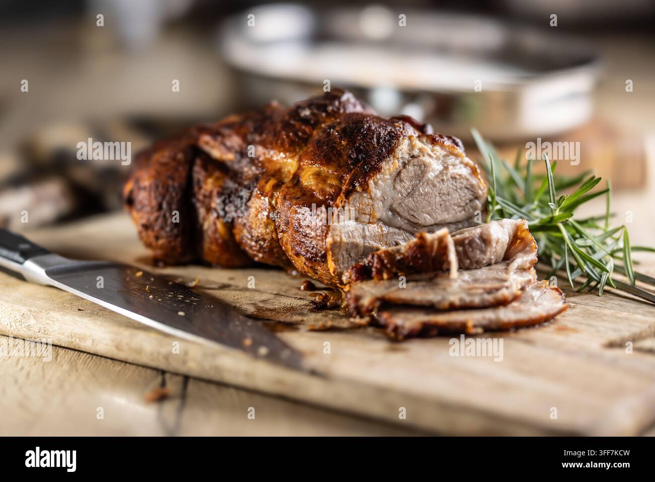 Leckeres gebratenes Schweinehals mit knuspriger Kruste ist mit frischem Rosmarin garniert und auf einem Holzbrett filetiert. Dieser professionelle kulinarische Shot wird pass Stockfoto