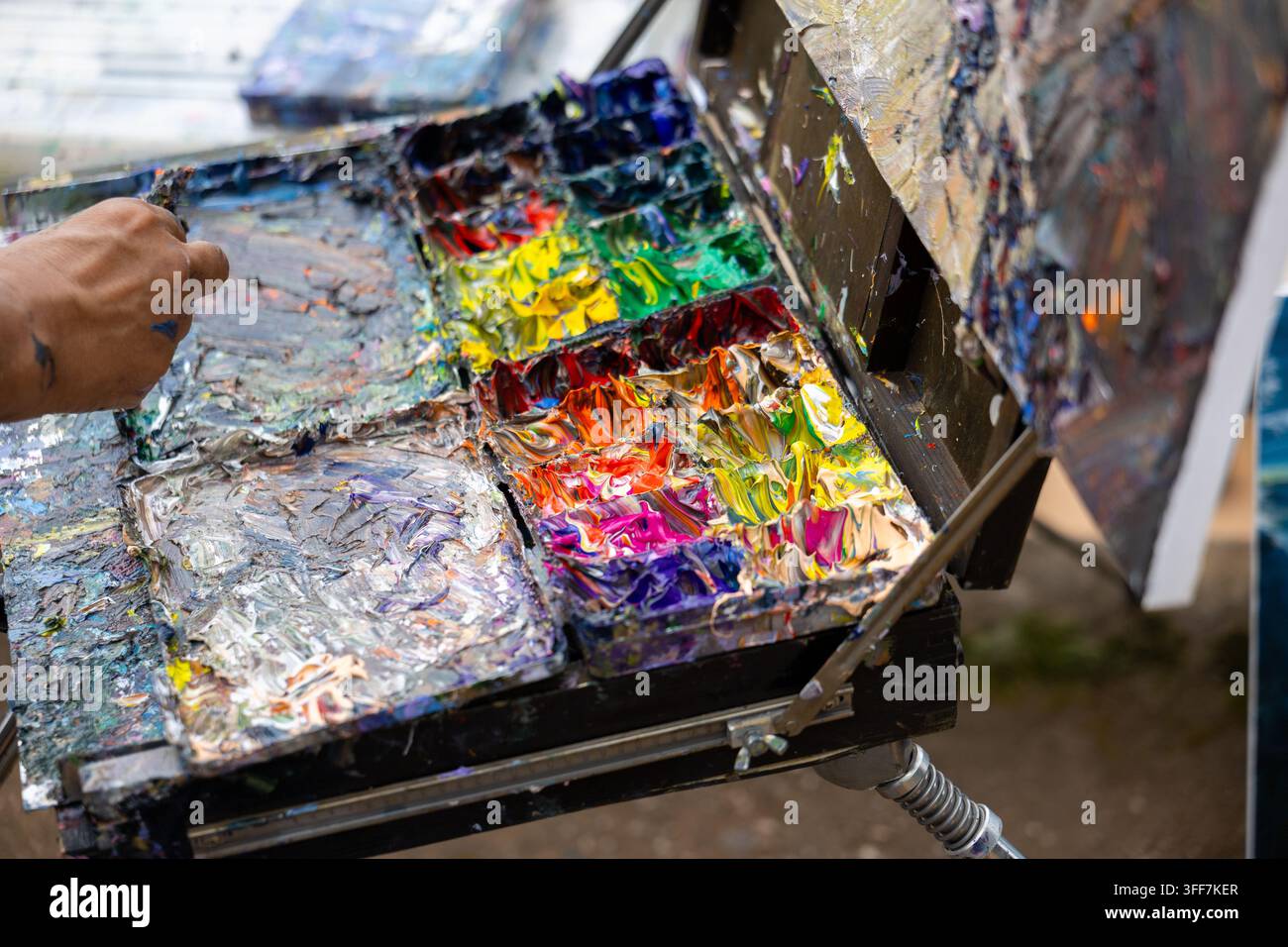 Eine farbenfrohe Farbpalette, Künstlerhand, die lebendige Ölfarbe im Studio mischt, Nahaufnahme eines kreativen Kunstwerkzeugs mit schmutziger Textur und Pinselstrich in der Werkstatt Stockfoto
