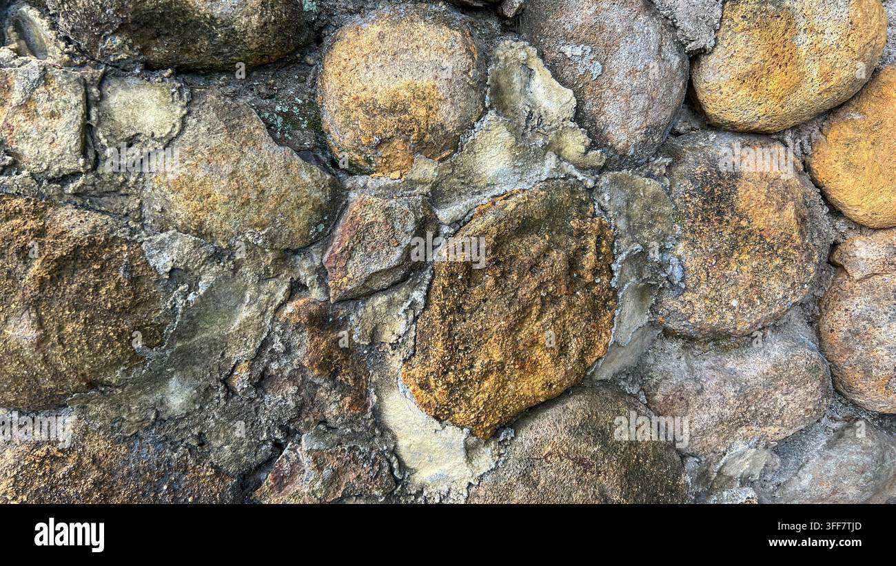 Nahaufnahme einer natürlichen Steinmauer mit hellbraunen und grauen Steinen und einer rauen, texturierten Mauerfläche, geeignet für architektonische und Hintergrundanwendungen Stockfoto