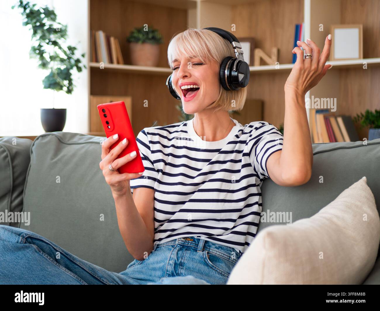 Glückliche junge Frau hört ihre Lieblingsplaylist über drahtlose Kopfhörer, während sie ihr Telefon benutzt. Stockfoto