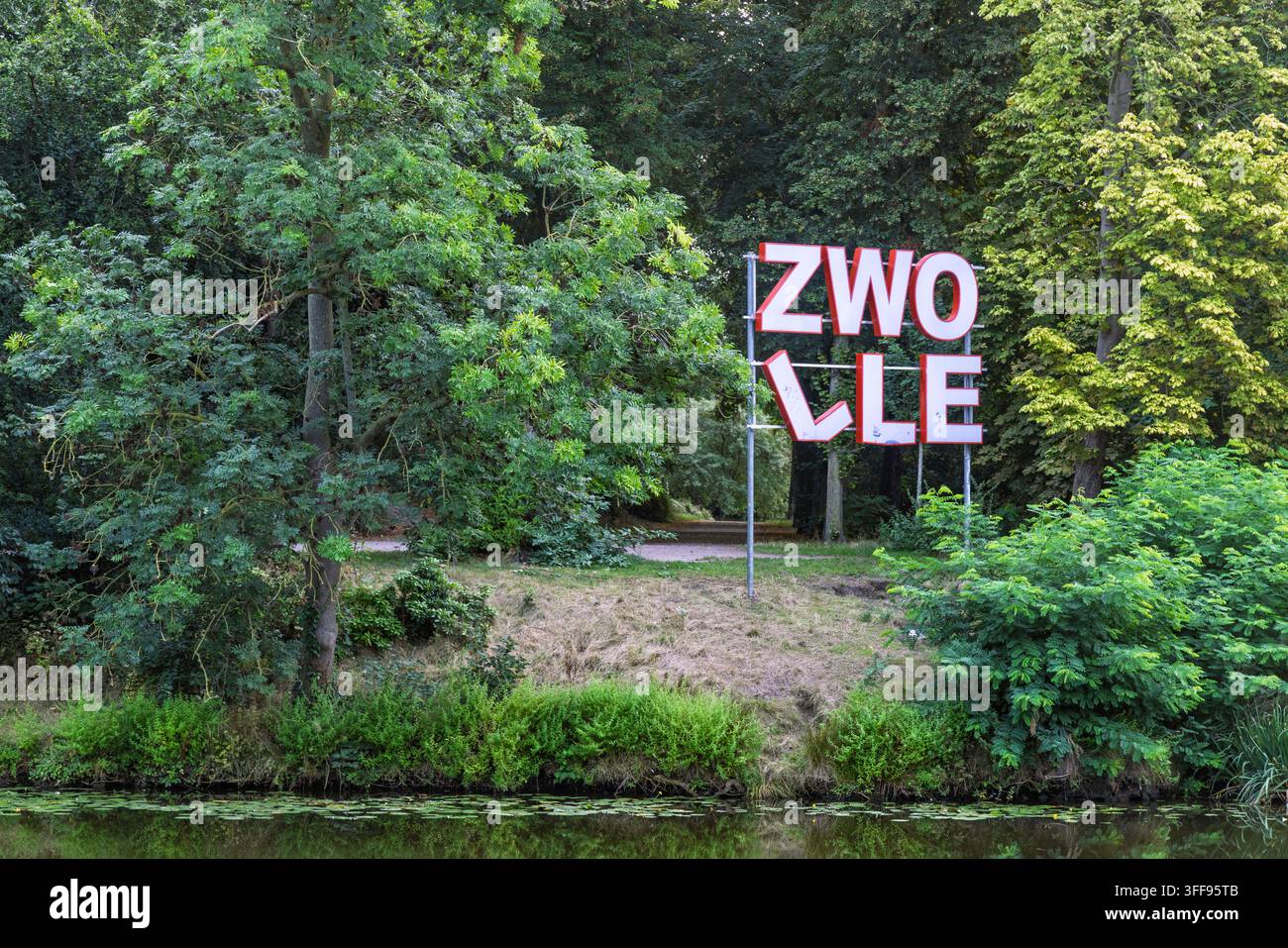 Zwolle, Niederlande – 23. August 2026: Ein großes, modernes rotes und weißes Stadtnamensschild von Zwolle, das in einer üppigen grünen Parkanlage neben einem Teich oder einer Dose steht Stockfoto
