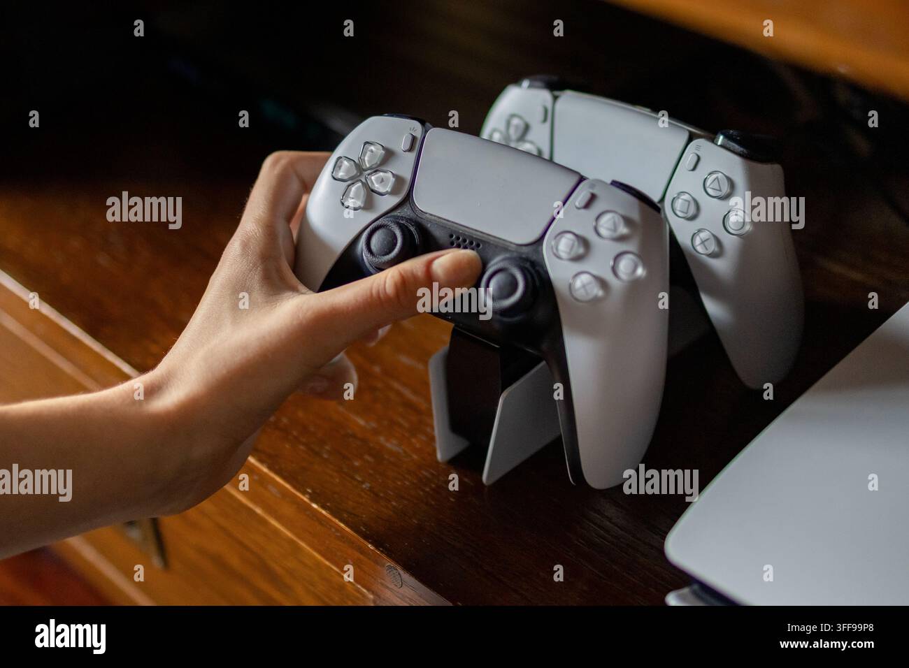 Bialystok, Polen – 5. Juli 2026: Hand verbindet zwei Sony PlayStation 5-Controller auf einem Holztisch zum Aufladen. Redaktionskonzept von DualSense Contro Stockfoto