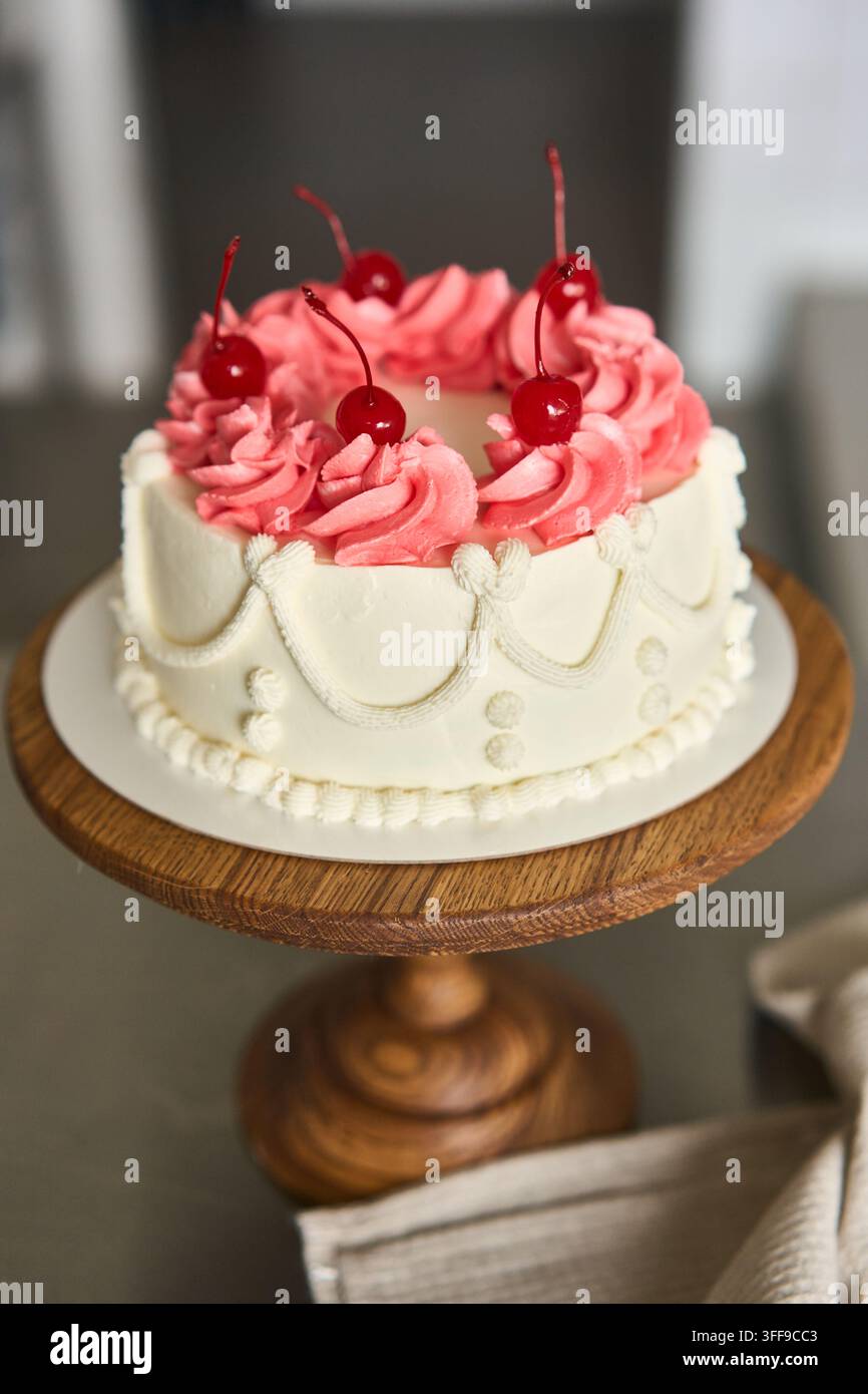 Runder Festkuch mit rosa Buttercreme-Rosetten und Maraschino-Kirschen auf rustikalem Holzsockel, mit Kuchen, Dessert, Buttercreme, Glasur Stockfoto