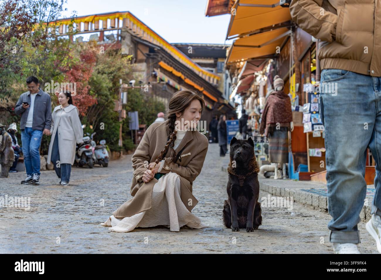 Frau kniet nieder, um einen Hund auf einer Kopfsteinpflasterstraße in der Altstadt von Shangri-La zu begrüßen Stockfoto