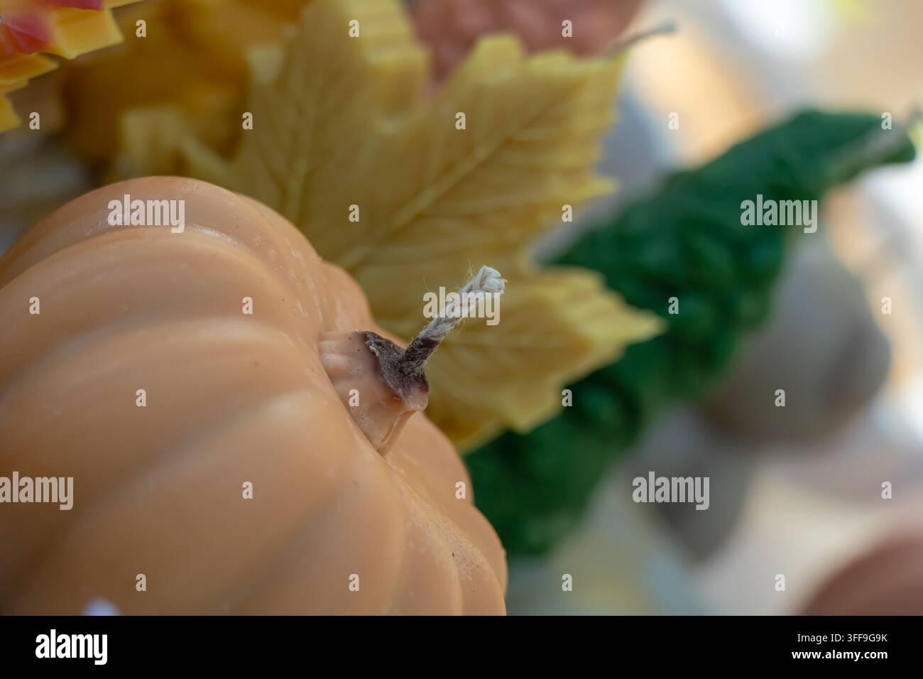 Nahaufnahme einer kerzenförmigen Kürbislaterne mit sichtbarem Baumwoll-Docht, eingerahmt von dekorativen Herbstblättern und warmen saisonalen Elementen im weichen Fokus. Stockfoto