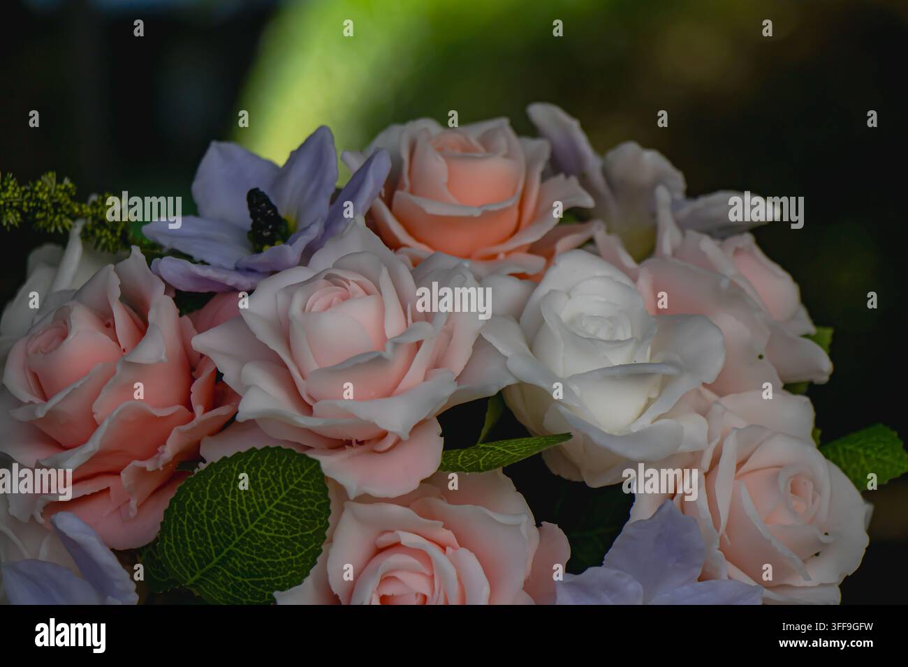 Nahaufnahme von künstlichen rosafarbenen und weißen Rosen mit blassvioletten Blumen und grünen Blättern, arrangiert vor einem dunklen Hintergrund für romantische Blumendekoration Stockfoto