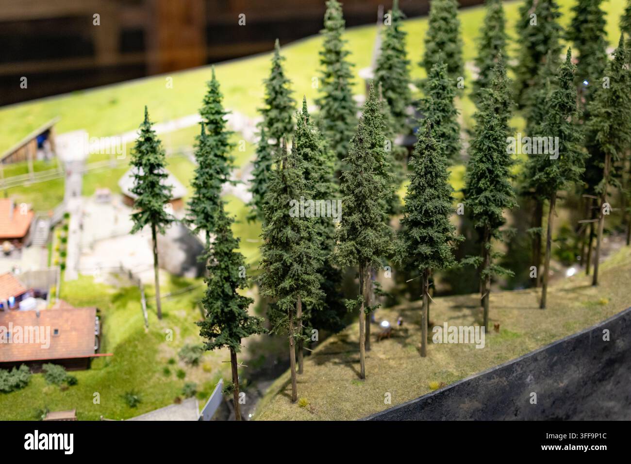 Gruppierte Fichtenkulissen erheben sich auf einem sonnigen Damm über den Dächern. Die sorgfältig gebaute Szenerie ruft mit texturierten Stämmen eine Bergwaldstimmung hervor, weich Stockfoto