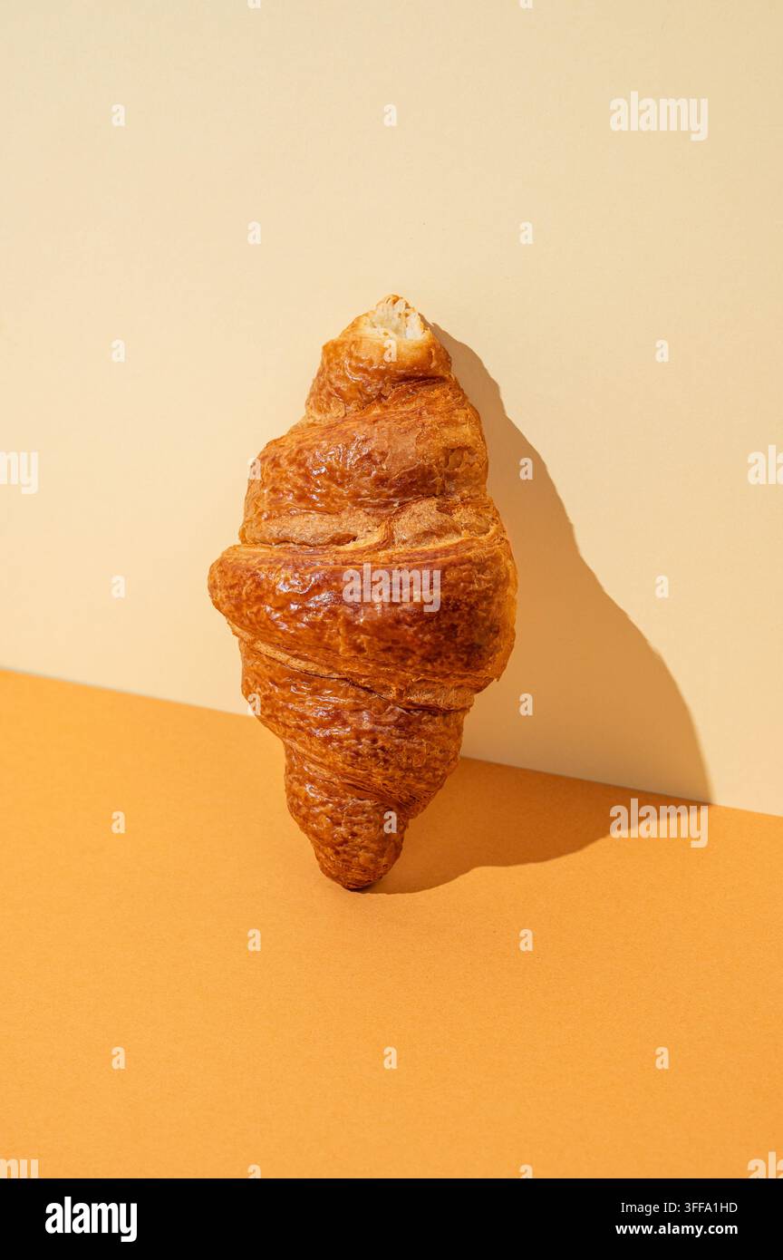 Frisches Croissant auf gelbem und orangefarbenem Hintergrund mit hartem Schatten. Kreatives diagonales trendiges Layout und gesundes Essen oder französisches Frühstückskonzept. Kopie s Stockfoto