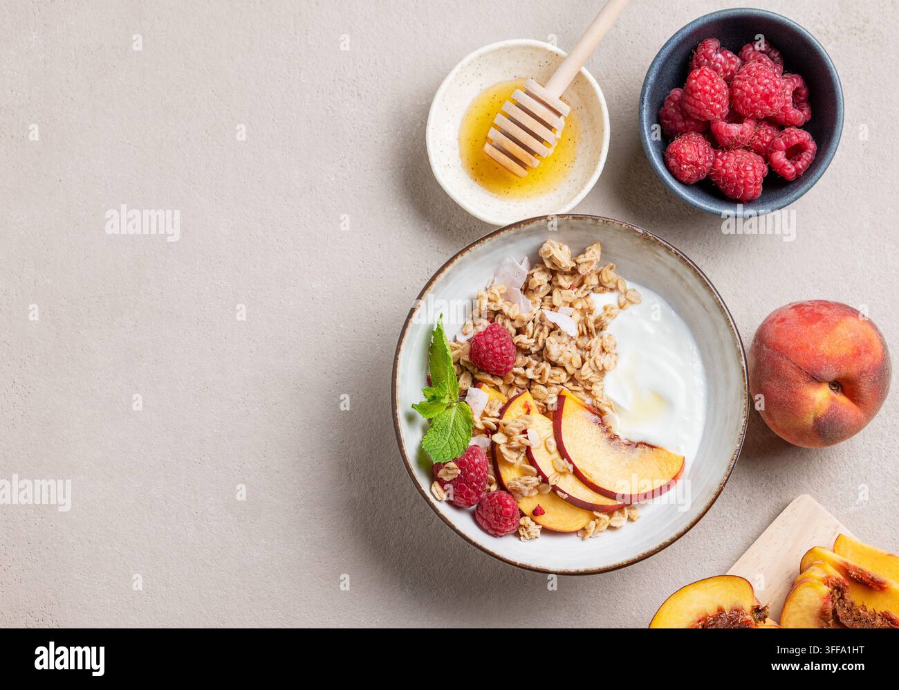 Flachlegung von griechischem Naturjoghurt mit Hafergranola oder Müsli, Pfirsich, Himbeere und Honig in einer Schüssel auf hellem Hintergrund mit frischen Früchten und Beeren. Stockfoto