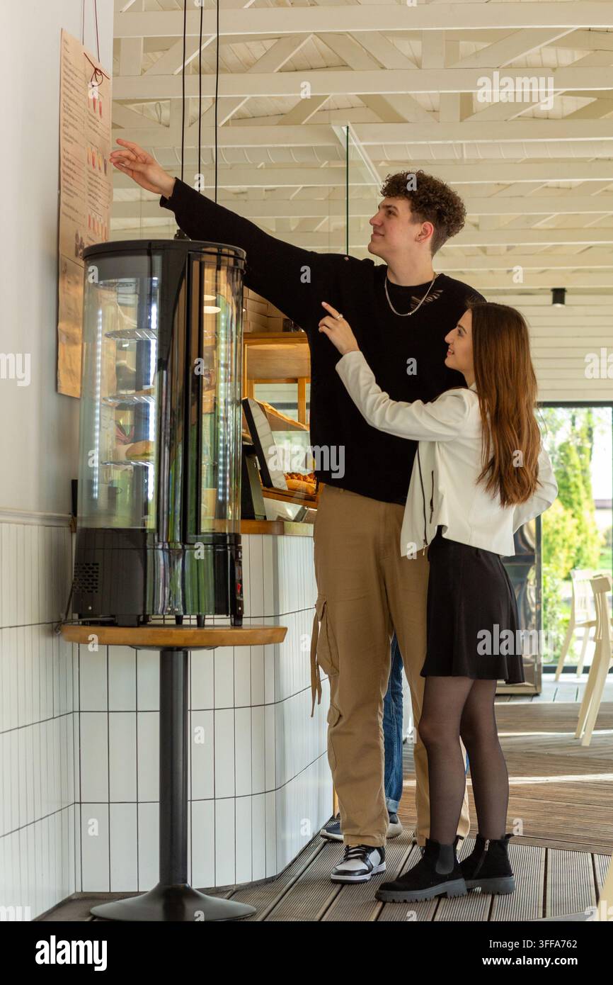 Junges Paar wählt Essen von einer Wandkarte an einem modernen Café-Tresen während eines lockeren Indoor-Dates. Stockfoto