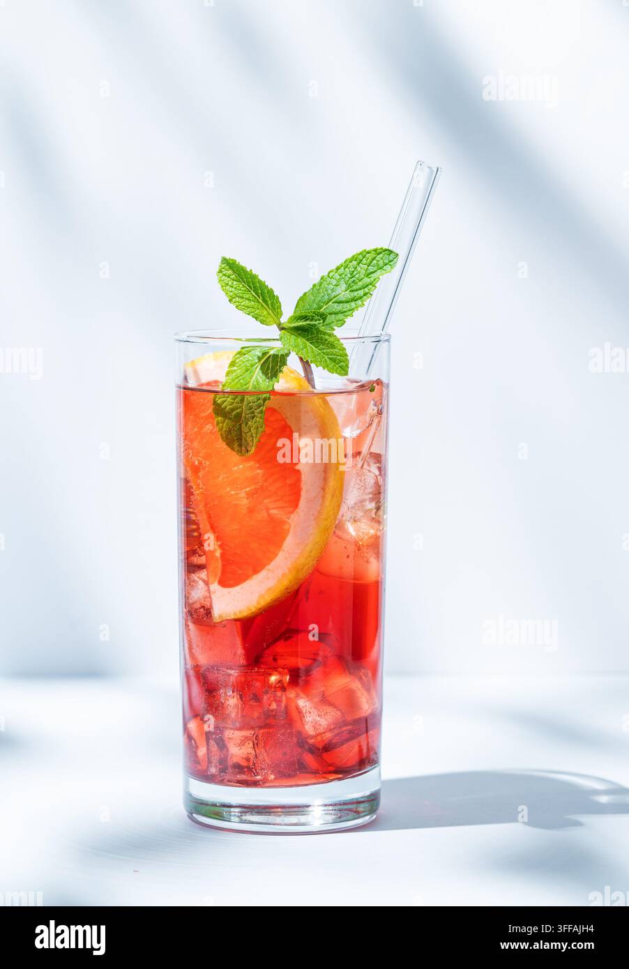 Erfrischender Cocktail mit Grapefruit, Minze und Eis in einem Glas auf hellem Hintergrund mit Schatten und Sonnenlicht. Sommer-Zitrusgetränk oder Limonade-Konzept. Stockfoto