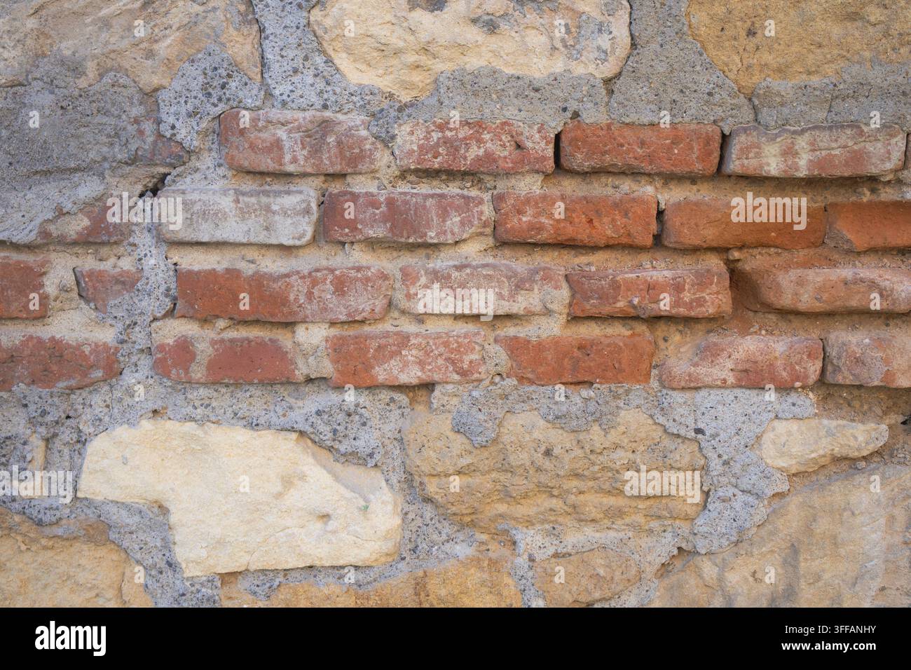 Verwitterte rote Ziegel, die in einer rauen Stein- und Mörtelmauer eingebettet sind Stockfoto