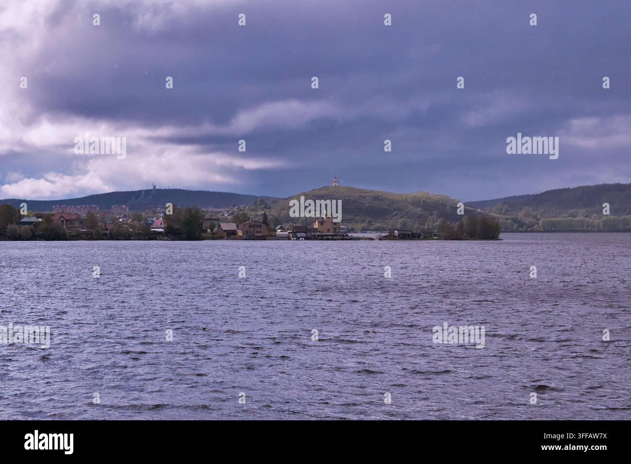 Ein Boot segelt friedlich auf einem ruhigen See, mit einem fernen Haus, das sich zwischen üppigen grünen Hügeln unter einem teilweise bewölkten Himmel befindet. Die Szene strahlt eine ruhige und t Stockfoto