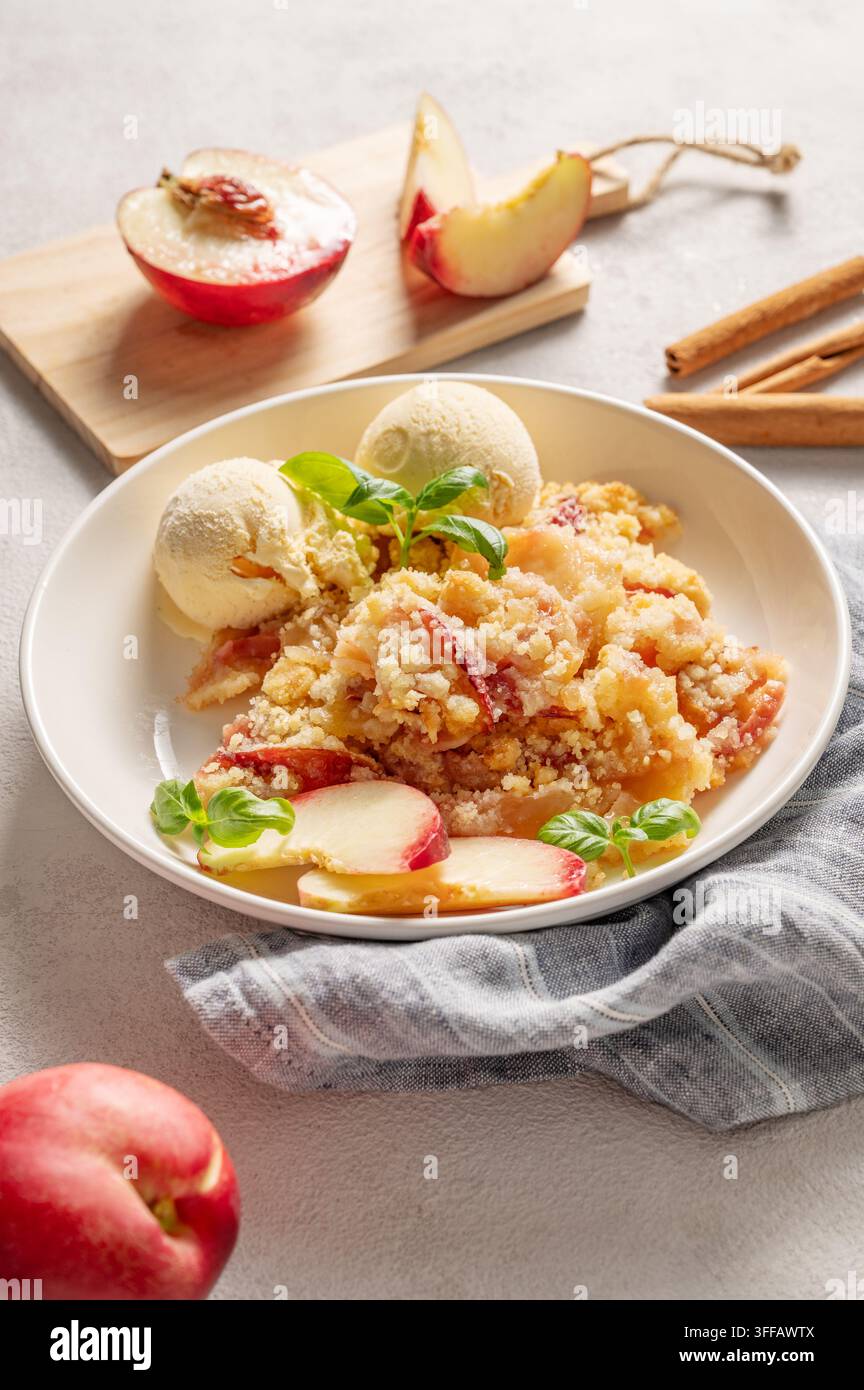 Pfirsich-Crumble oder -Cobbler mit Vanilleeis-Scoops und Zimt auf einem Teller vor einem hellen Hintergrund mit frischen Früchten. Sommerliches hausgemachtes erfrischendes Dessert Stockfoto