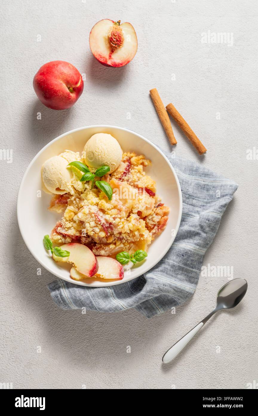 Pfirsich-Crumble oder -Cobbler mit Vanilleeis-Scoops und Zimt auf einem Teller vor einem hellen Hintergrund mit frischen Früchten. Sommerliches hausgemachtes erfrischendes Dessert Stockfoto
