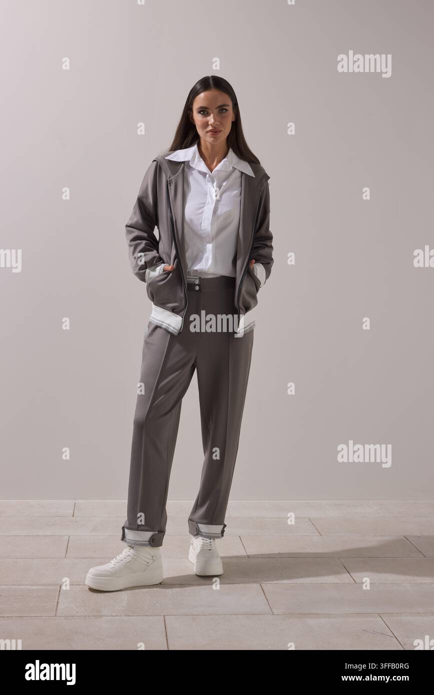 Junge brünette Frau trägt einen grauen Oversized-Blazer über einem weißen Hemd mit passenden grauen taillierten Weitbundhosen. Stockfoto