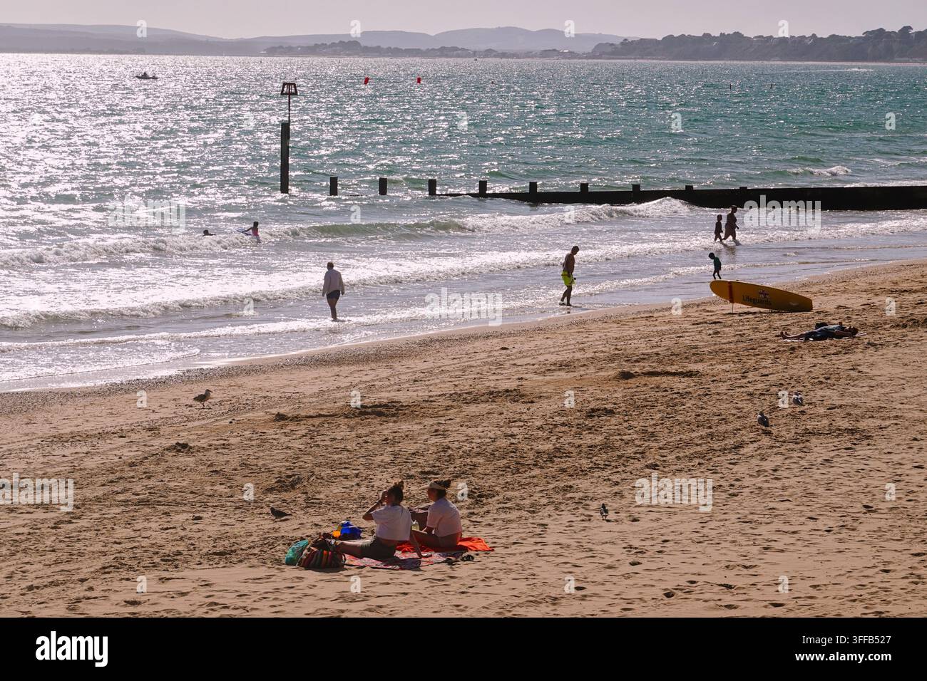 Panoramatische Ansicht des Sandstrands in Boscombe, Bournemouth, UK, mit Urlaubern, hölzernen Groynes und dem Bournemouth Pier in der Ferne. Stockfoto