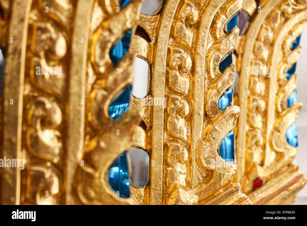 Goldenes Stuckrelief mit blauen verspiegelten Glasintarsien an einer thailändischen buddhistischen Tempelmauer in Thailand, Nahaufnahme eines architektonischen Details Stockfoto