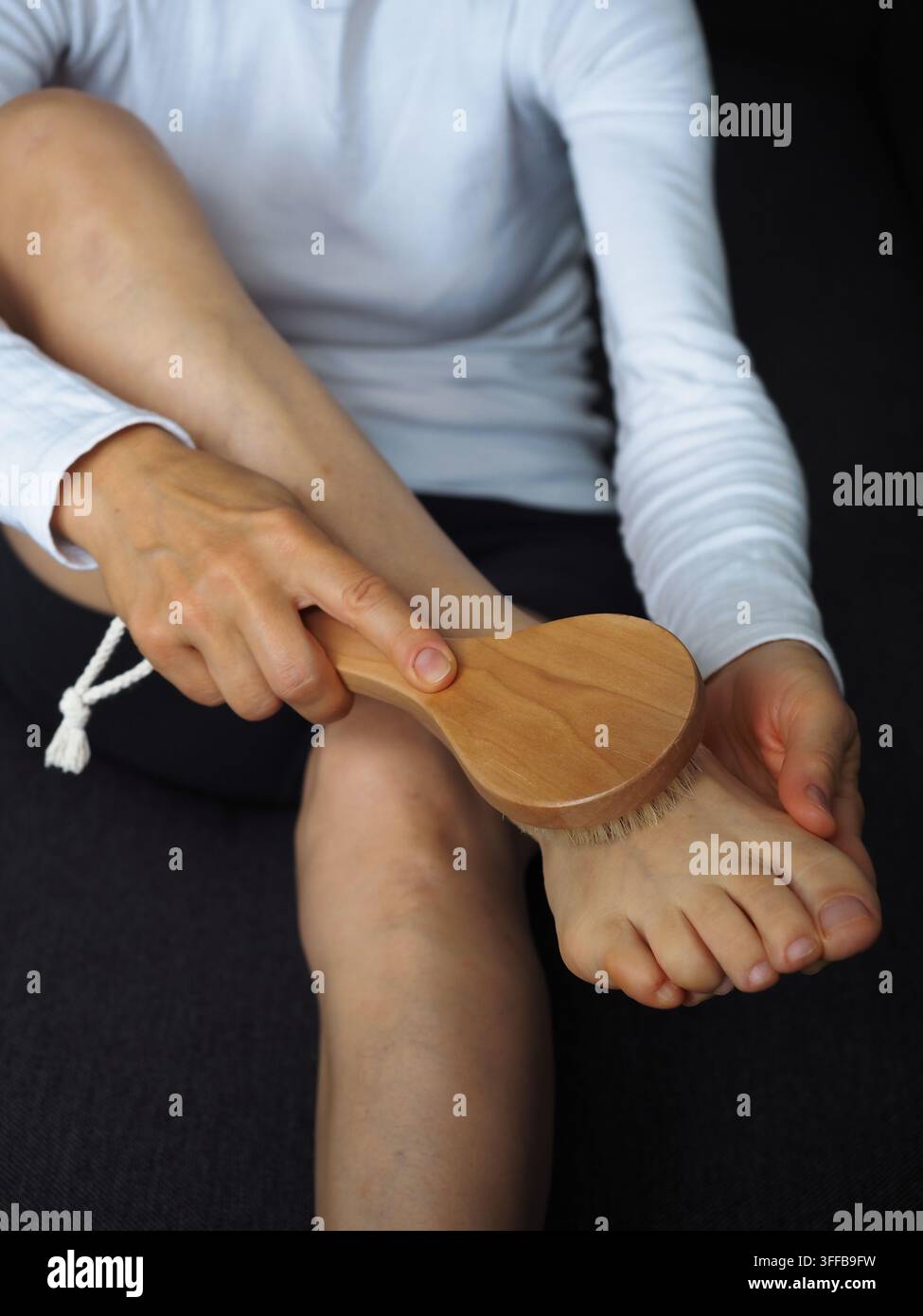 Frau übt trockenes Körperbürsten an ihrem Fuß mit einer natürlichen Holzbürste Stockfoto