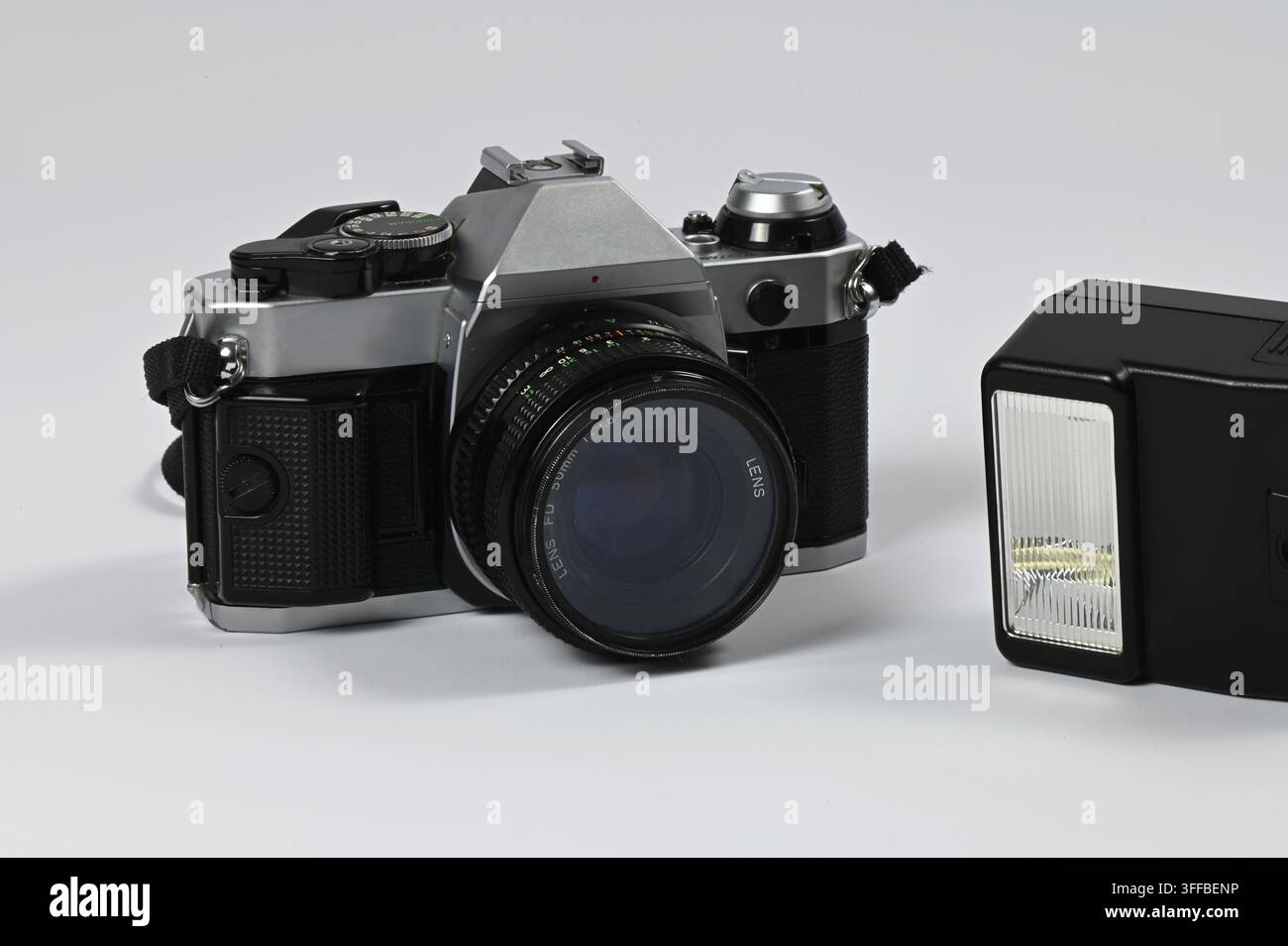 Eine alte analoge Kamera mit einem Körper aus Metall und schwarzem Kunststoff ruht auf einem weißen Hintergrund. Neben der Kamera befindet sich eine abnehmbare Blitz-Einheit. Stockfoto