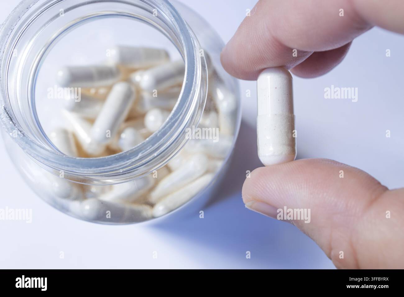 Hand, die eine weiße Kapsel neben einem offenen Gläser mit Pillen hält, Medikamentenkonzept Stockfoto