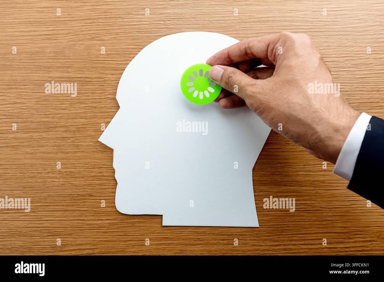 Geschäftsmann legt ein grünes Lade-Symbol auf einen papiernen menschlichen Kopf. Konzept für Unternehmensausburnout, mentale Erschöpfung, langsame kognitive Verarbeitung. Stockfoto