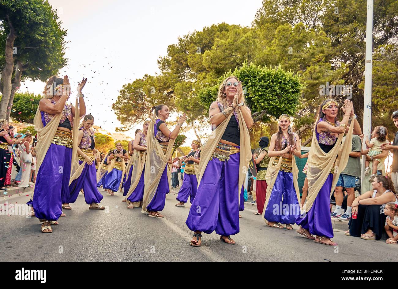 Frauen in lila und goldenen Kostümen heben ihre Hände, während Konfetti während einer Festumzugstraße in Santa Ponsa, Mallorca, fällt. Stockfoto