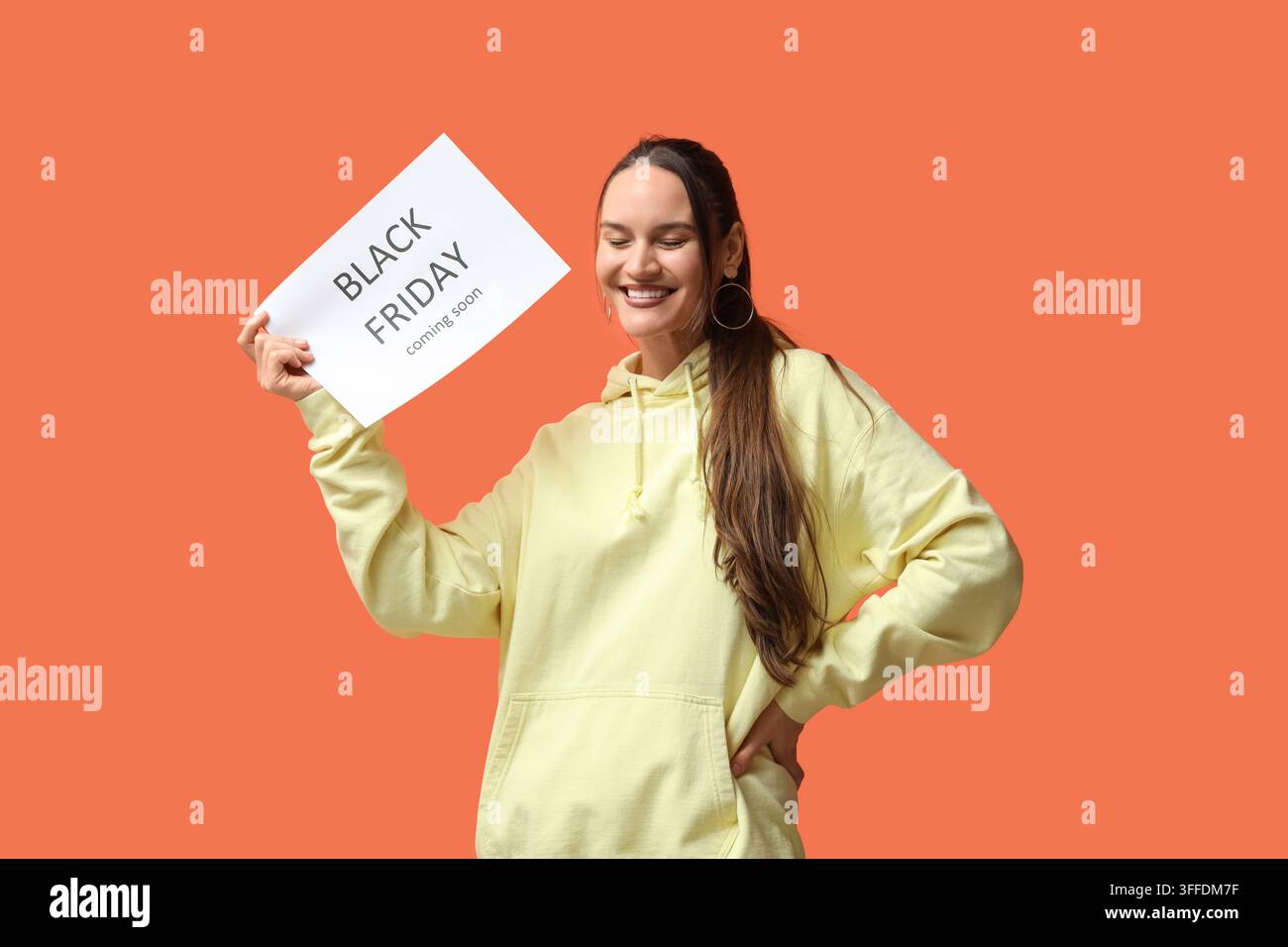 Fröhliche junge Frau hält ein Plakat mit dem Text BLACK FRIDAYS KOMMT BALD auf orangefarbenem Hintergrund Stockfoto