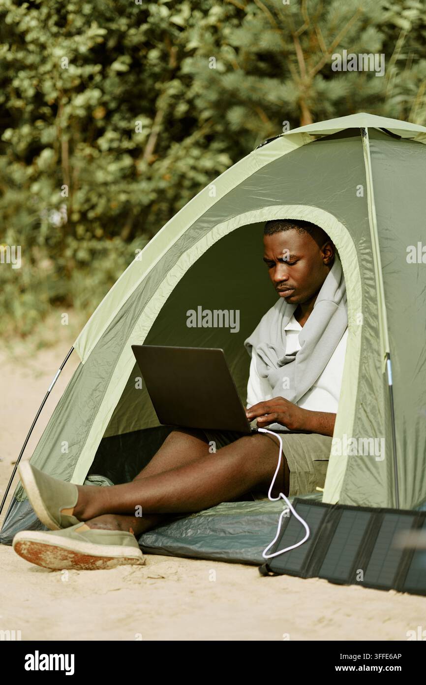 Schwarzer Mann arbeitet an einem Laptop im Zelt beim Camping im Freien Stockfoto