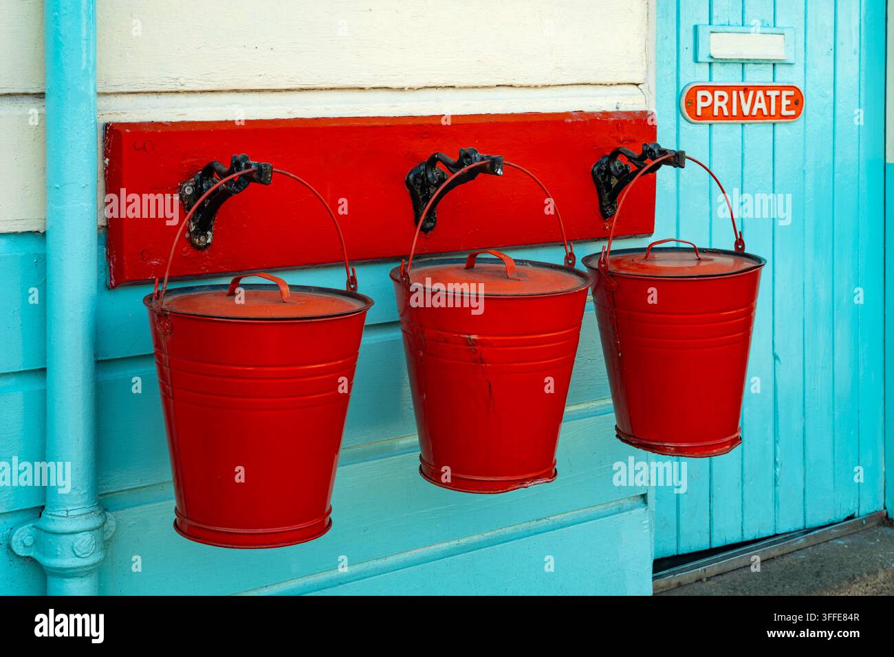 Drei alte rote Feueimädel hängen vor einem türkisfarbenen Holzstationgebäude in Grosmont, North Yorkshire, England. Stockfoto