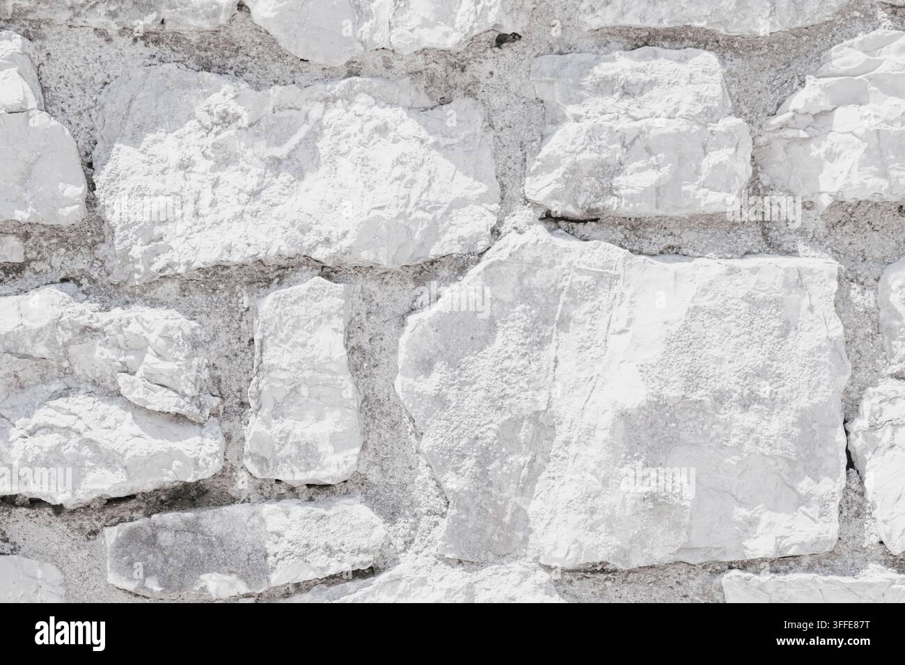 Nahaufnahme einer strukturierten weißen Steinmauer mit unregelmäßig geformten Steinen und sichtbaren Mörtelfugen, die eine rustikale und natürliche Ästhetik vermitteln Stockfoto