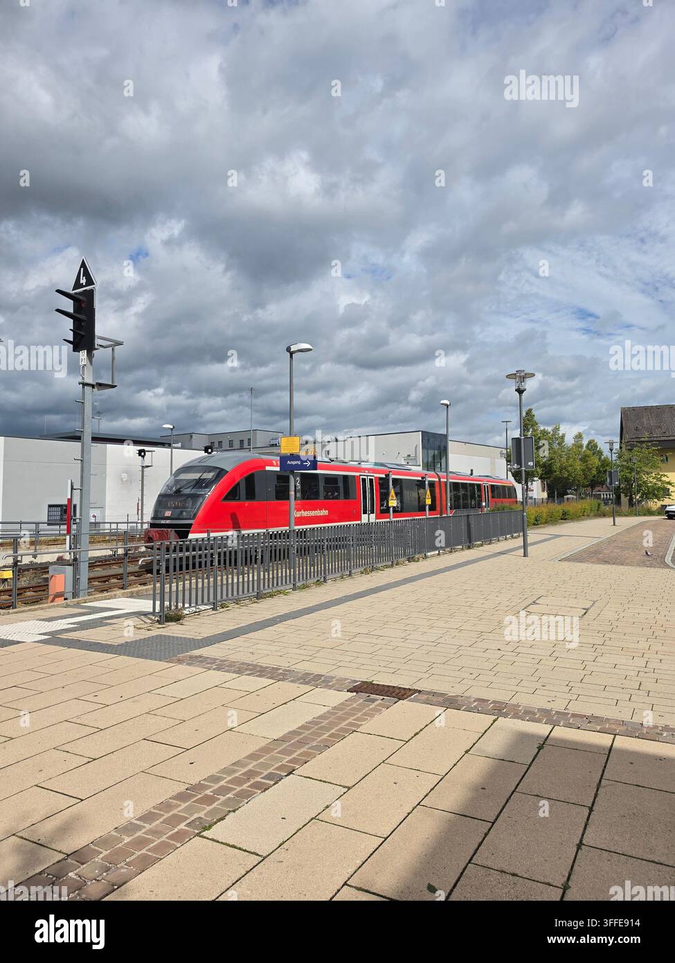 Roter Regionalzug auf einem Bahnsteig unter einem wolkigen grauen Himmel an einem Sommertag in Deutschland ( - Smartphone-aufgenommenes Stockfoto