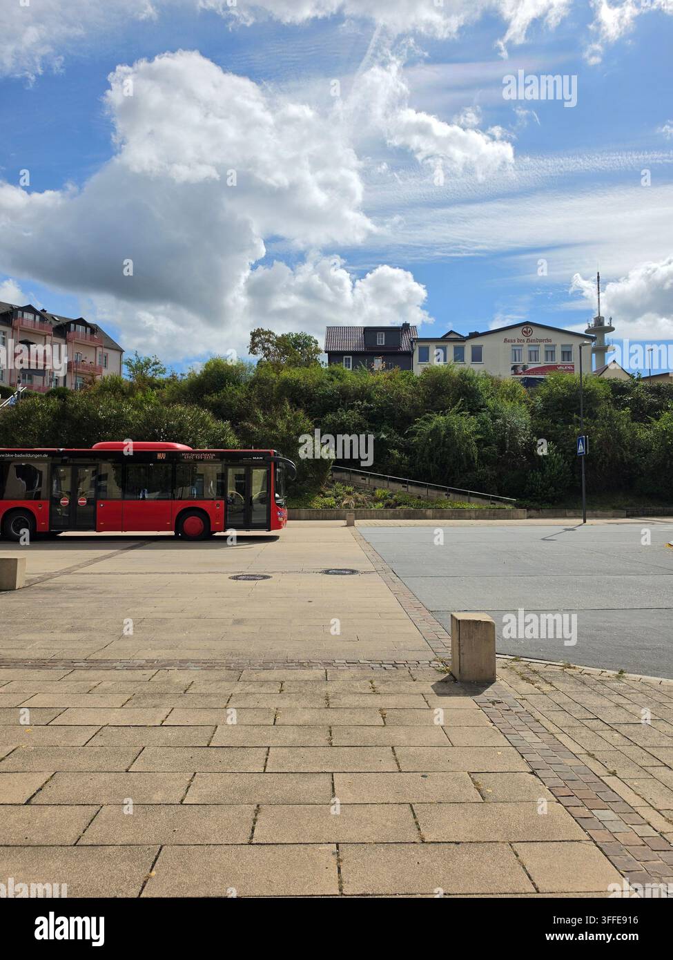 Roter öffentlicher Bus auf dem Stadtplatz mit Wohnhäusern auf dem Hügel und dramatischem bewölktem Himmel in Frankenberg Hessen Deutschland - Smartphone-aufgenommenes Stockfoto