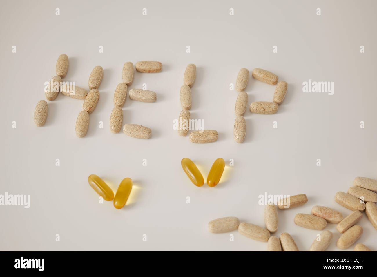 Beige Kapseln bilden das Wort HILFE auf einer weißen Oberfläche mit gelben durchsichtigen Kapseln und einer verstreuten Gruppe von Pillen in der Nähe. Gesundheitsunterstützung und Med Stockfoto