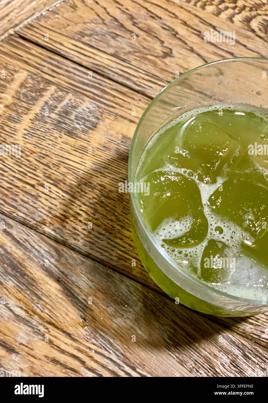 Eisgetränk in grüner Farbe in klarem Glas auf rustikalem Holztisch. Stockfoto